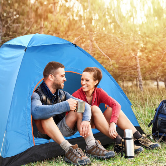 Blue pop up camping tent with two adults sitting inside at an outdoor campsite