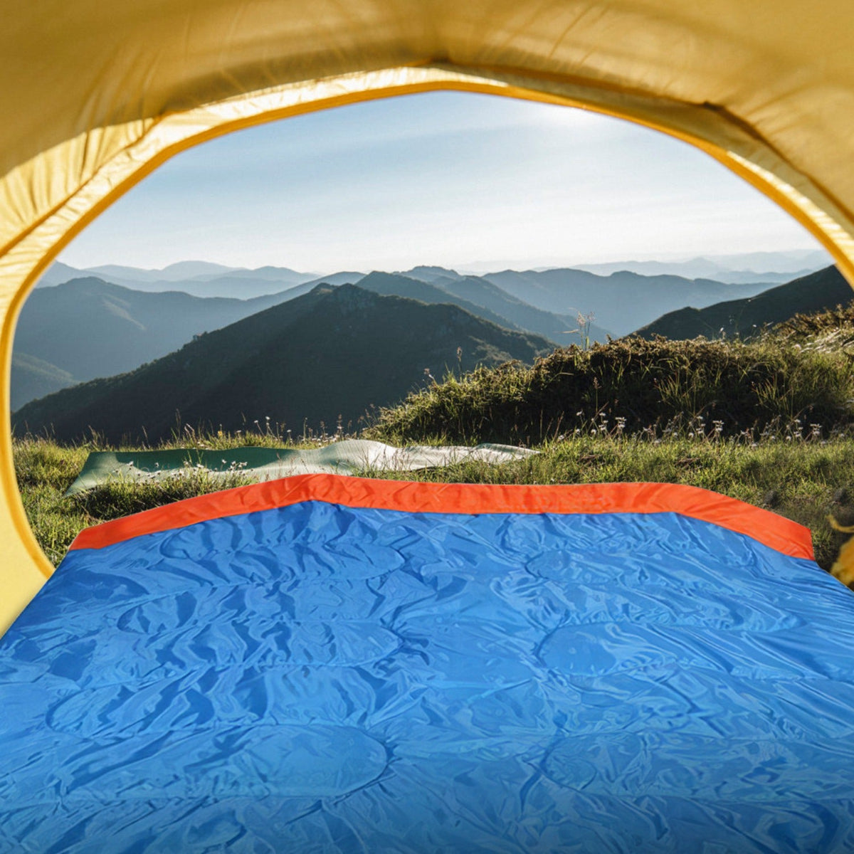 Camping scene with a tent and blue sleeping pad overlooking mountains.