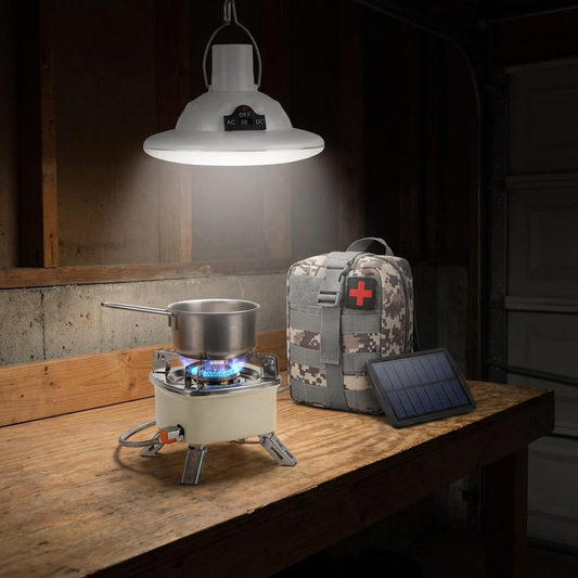 Portable stove with pot, camouflage first aid kit, and solar panel on a wooden table under a hanging light.