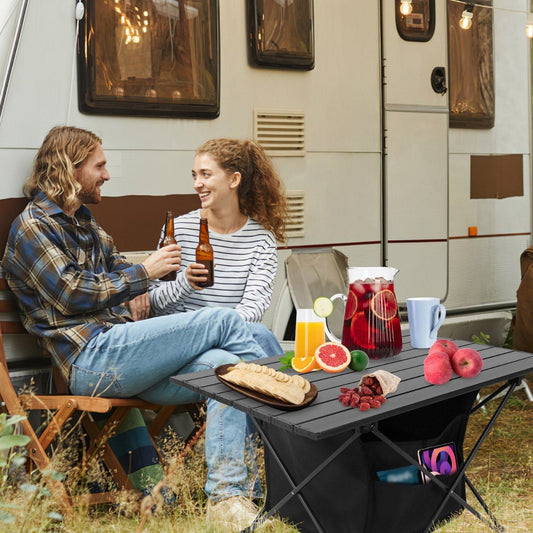 Camping table holding food and drinks in front of a parked travel trailer