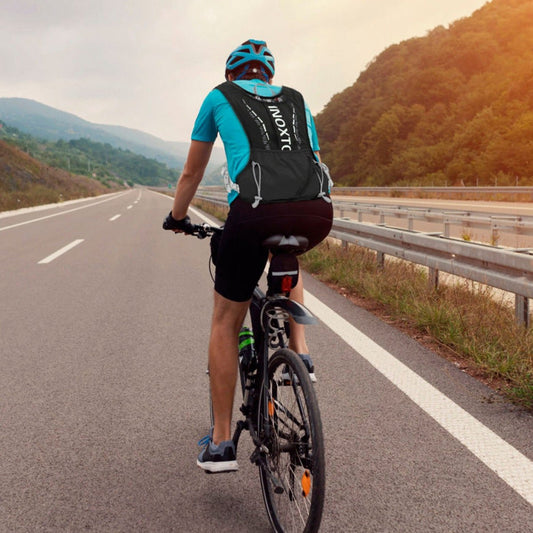 Person cycling on an open road wearing a black hydration vest, rear view