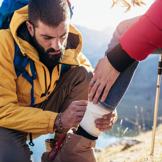 Person wrapping a bandage around an ankle during a mountain hike
