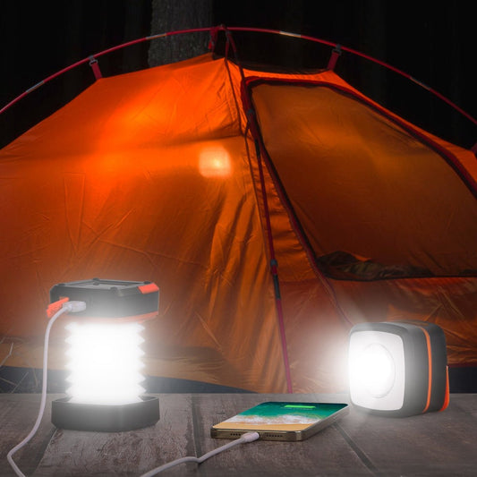 Lantern and cube light charging a phone on a table in front of a lit tent