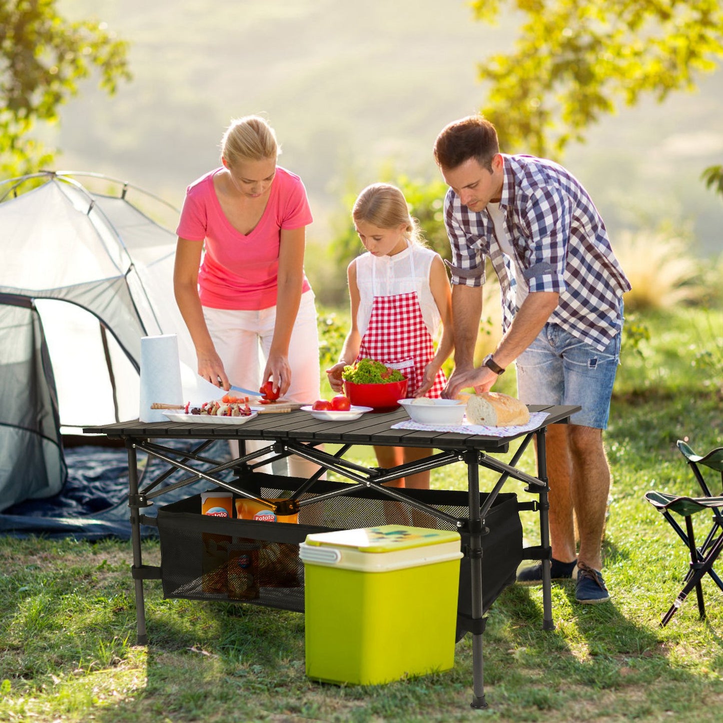 Family preparing food outdoors near a tent in a park
