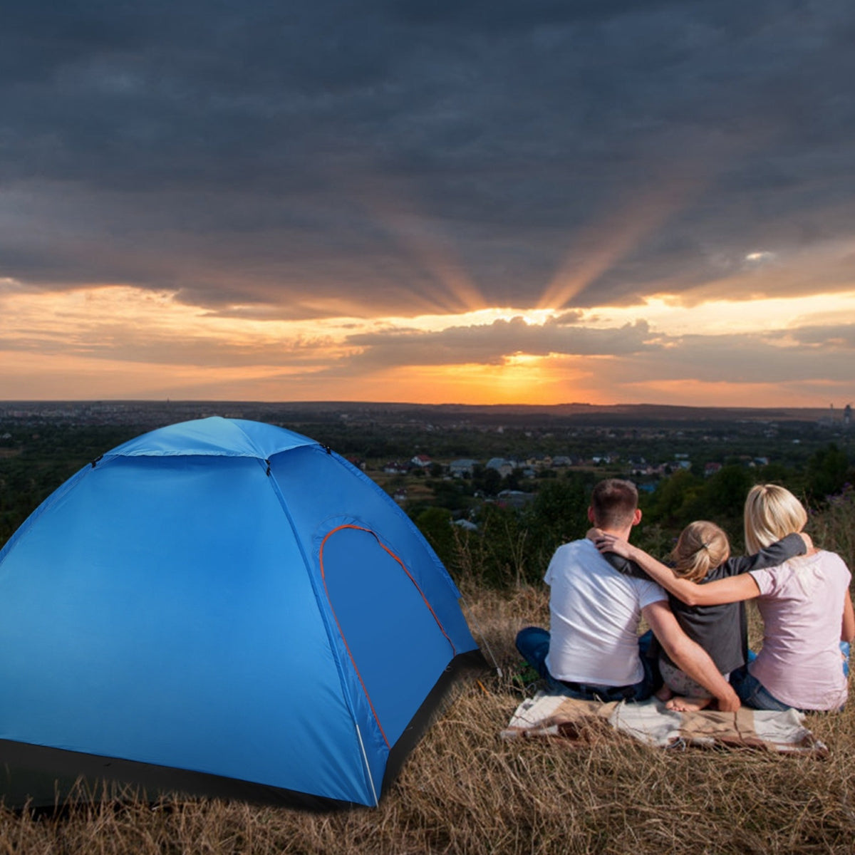 Blue pop up camping tent pitched on grassy ground overlooking an open landscape at sunset