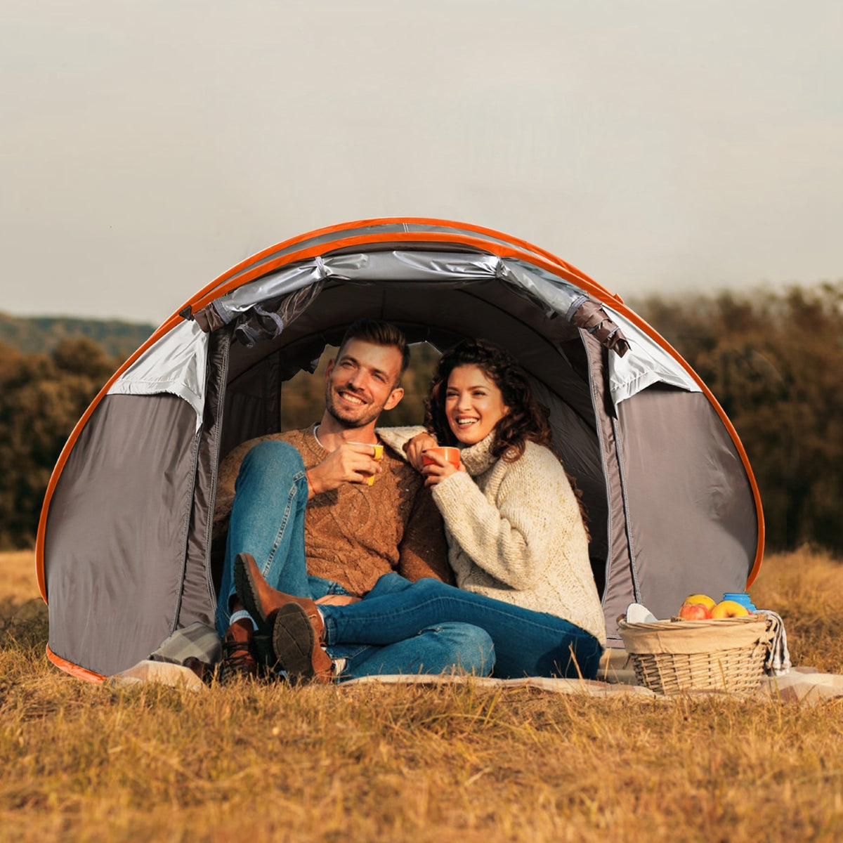 Two adults seated inside an open tent on grassy terrain outdoors