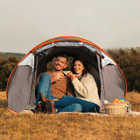 Two adults seated inside an open tent on grassy terrain outdoors