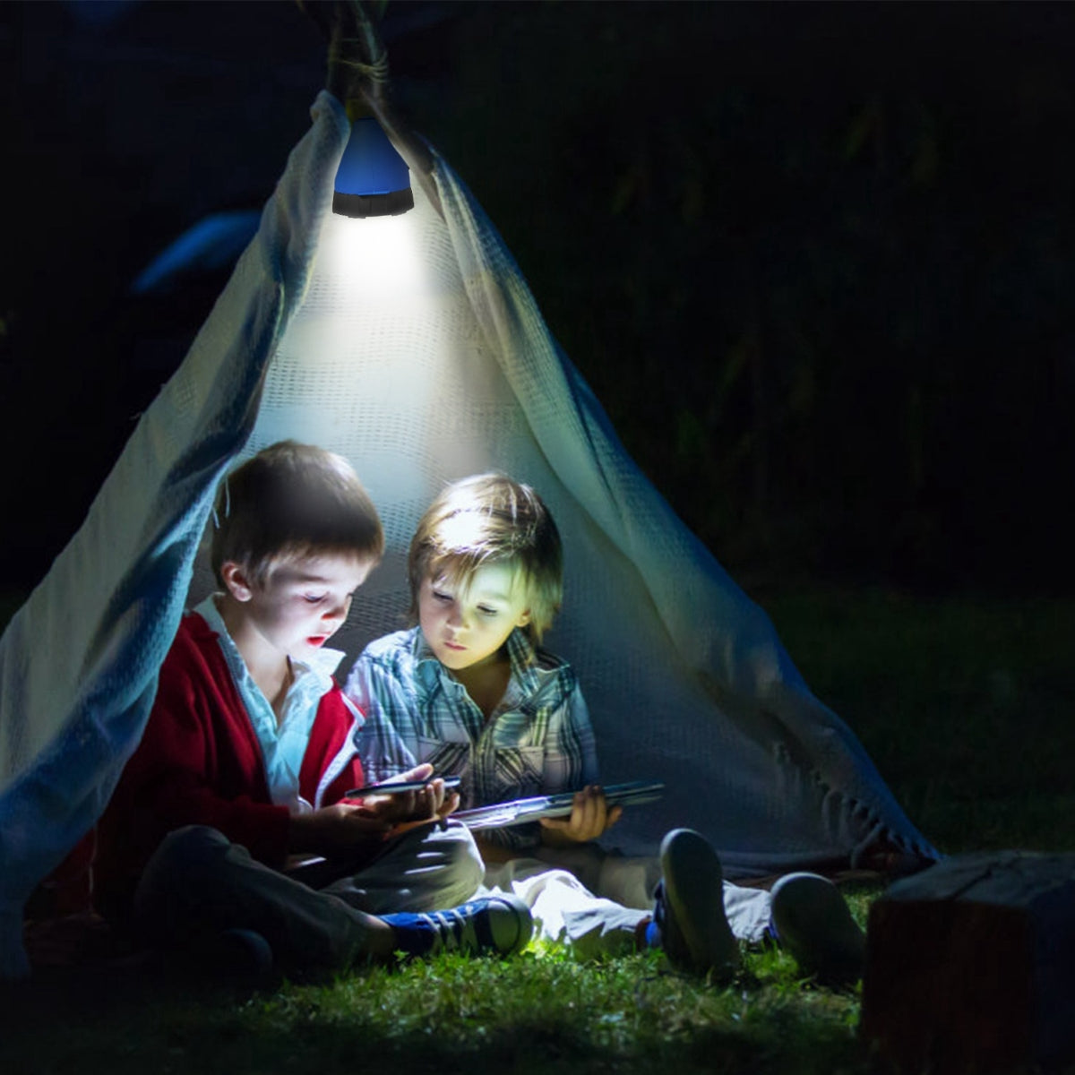 Camping lantern hanging above children seated under a blanket outdoors at night