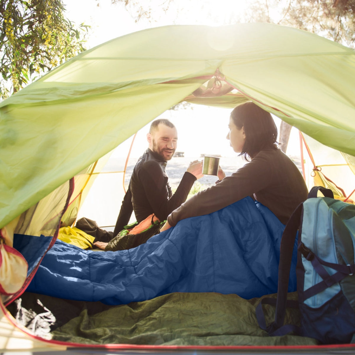 Two people sitting inside a tent with a sleeping bag spread on the floor