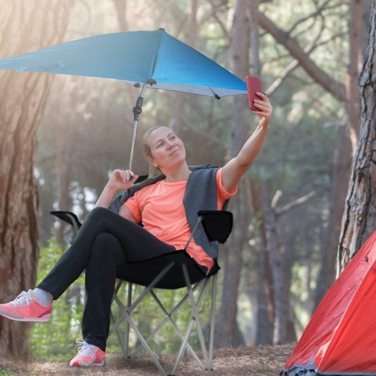 Person sitting in a camping chair under a blue canopy in a forest setting.