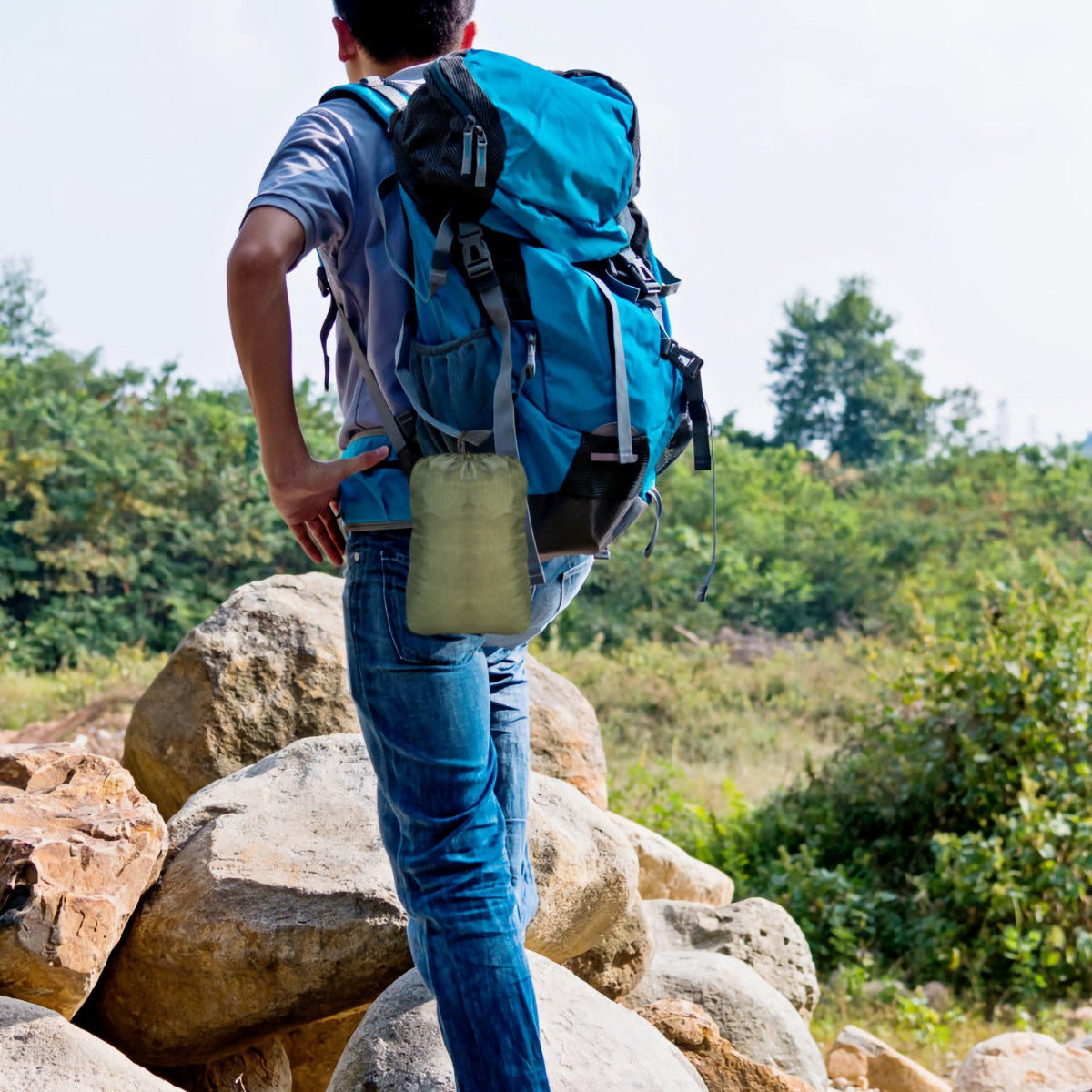 Person with a blue backpack standing on rocks with a natural landscape in the background