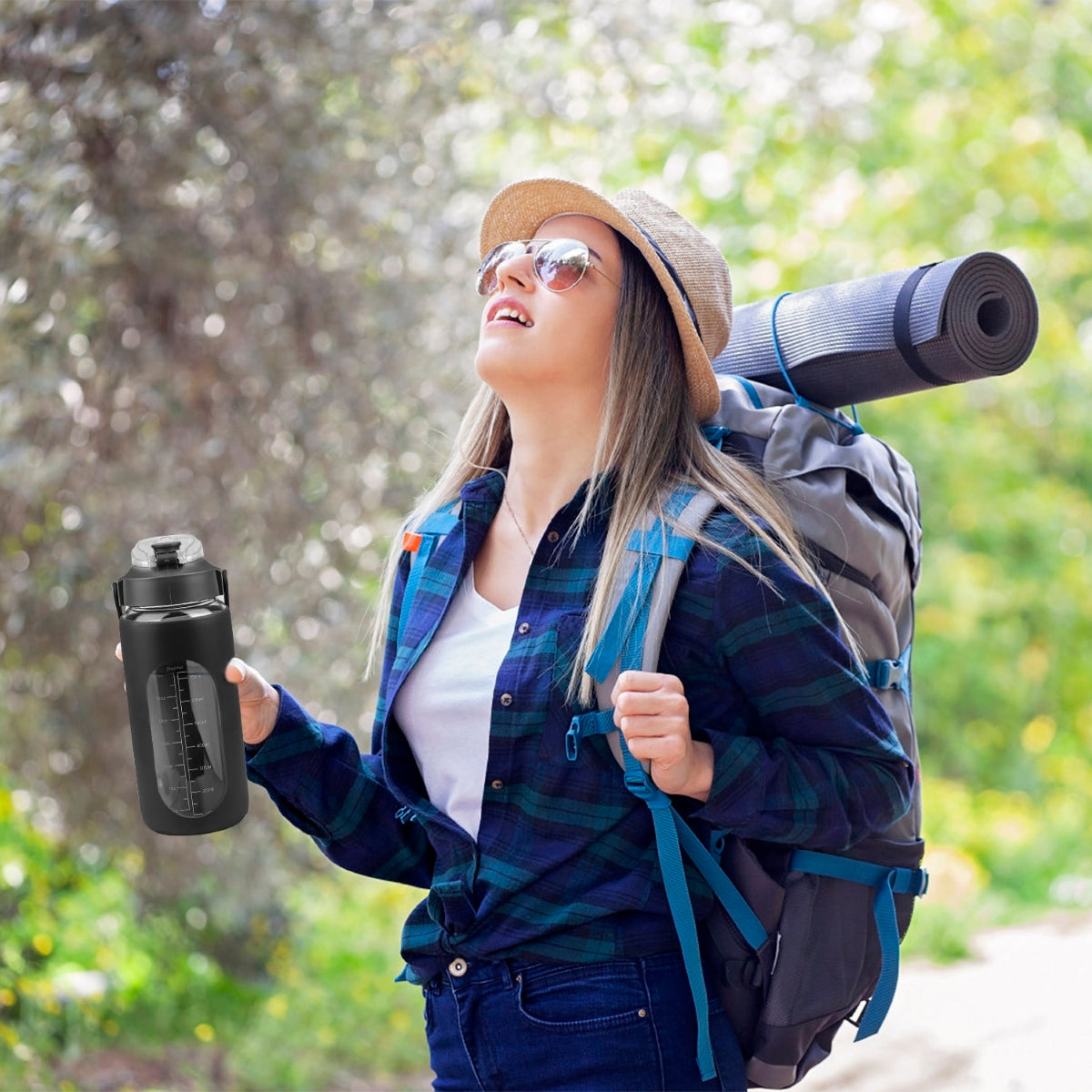 Hiker on forest trail holding black water bottle with backpack