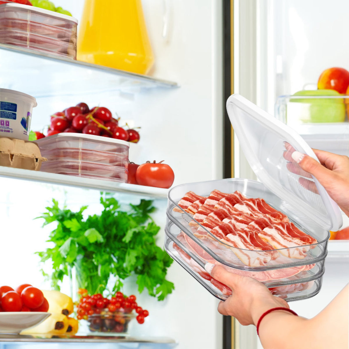 Stack of transparent food containers with meat held in front of an open refrigerator filled with food.