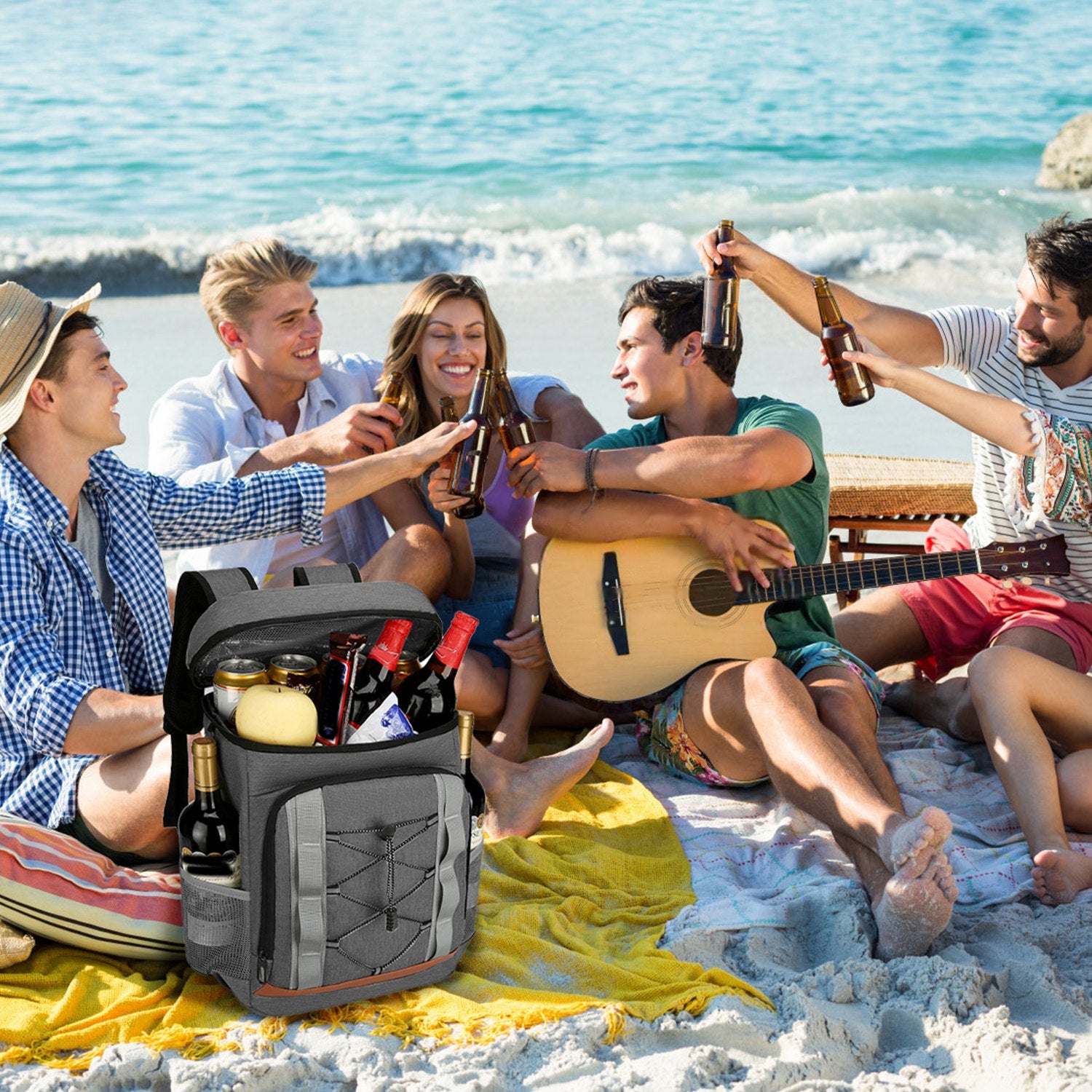 Group of friends enjoying a picnic on the beach with a guitar and drinks.