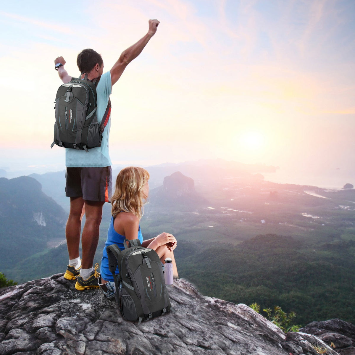 Two hikers with backpacks standing on a mountain peak with a scenic view.