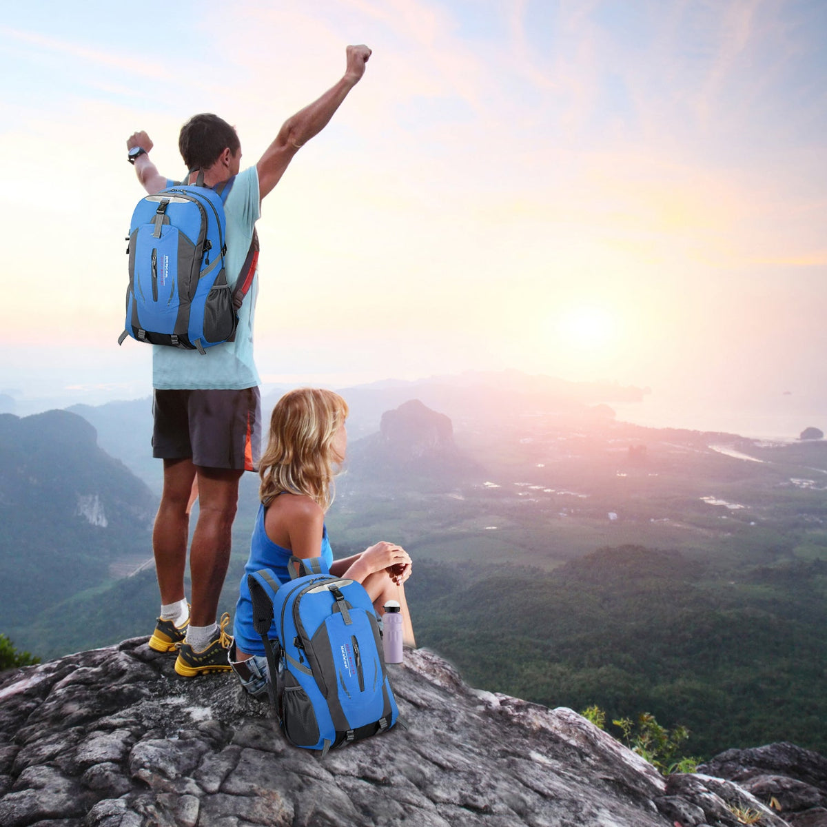 Two people with backpacks standing on a mountain top with a scenic view.