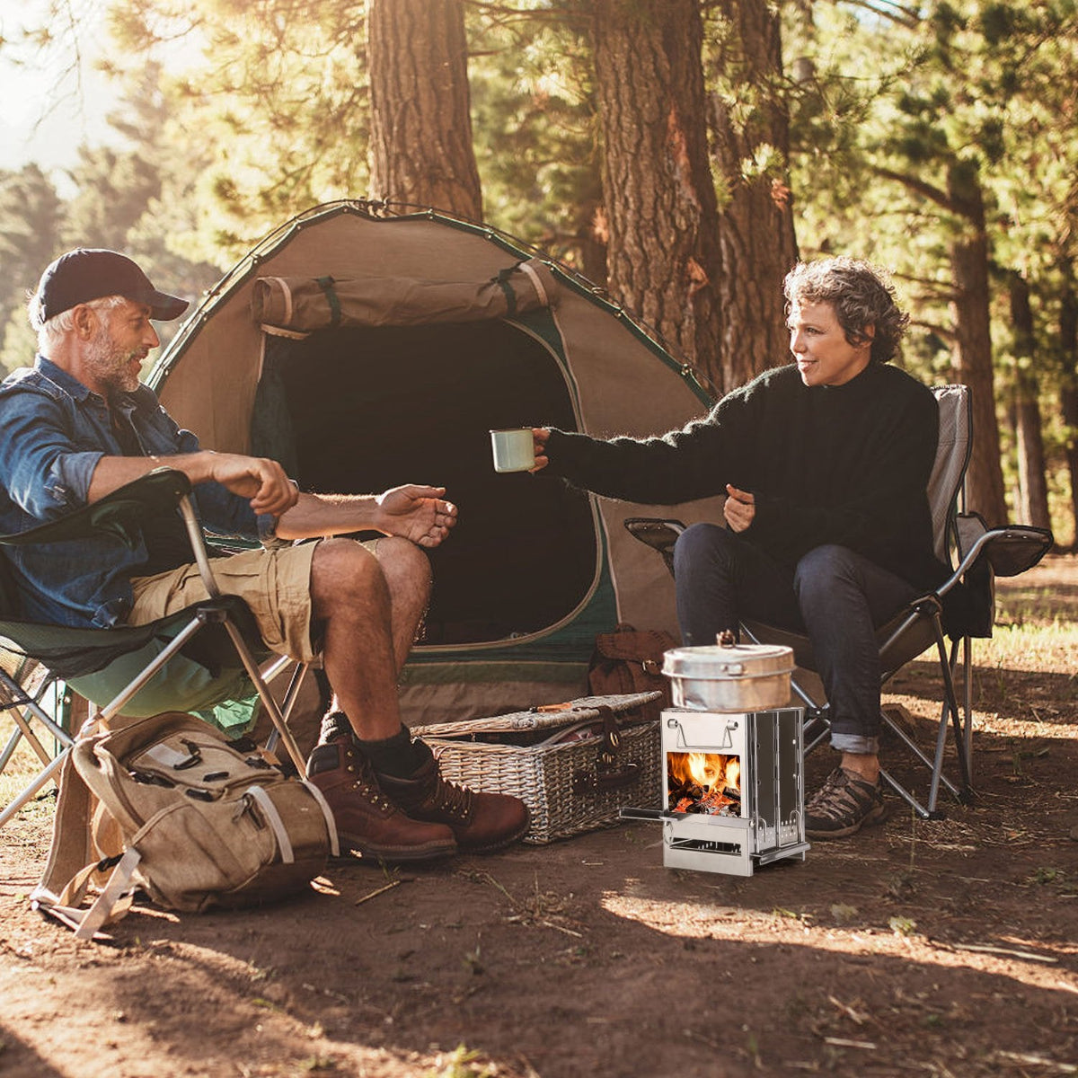 Two people camping in a forest, sitting by a portable stove with a fire.