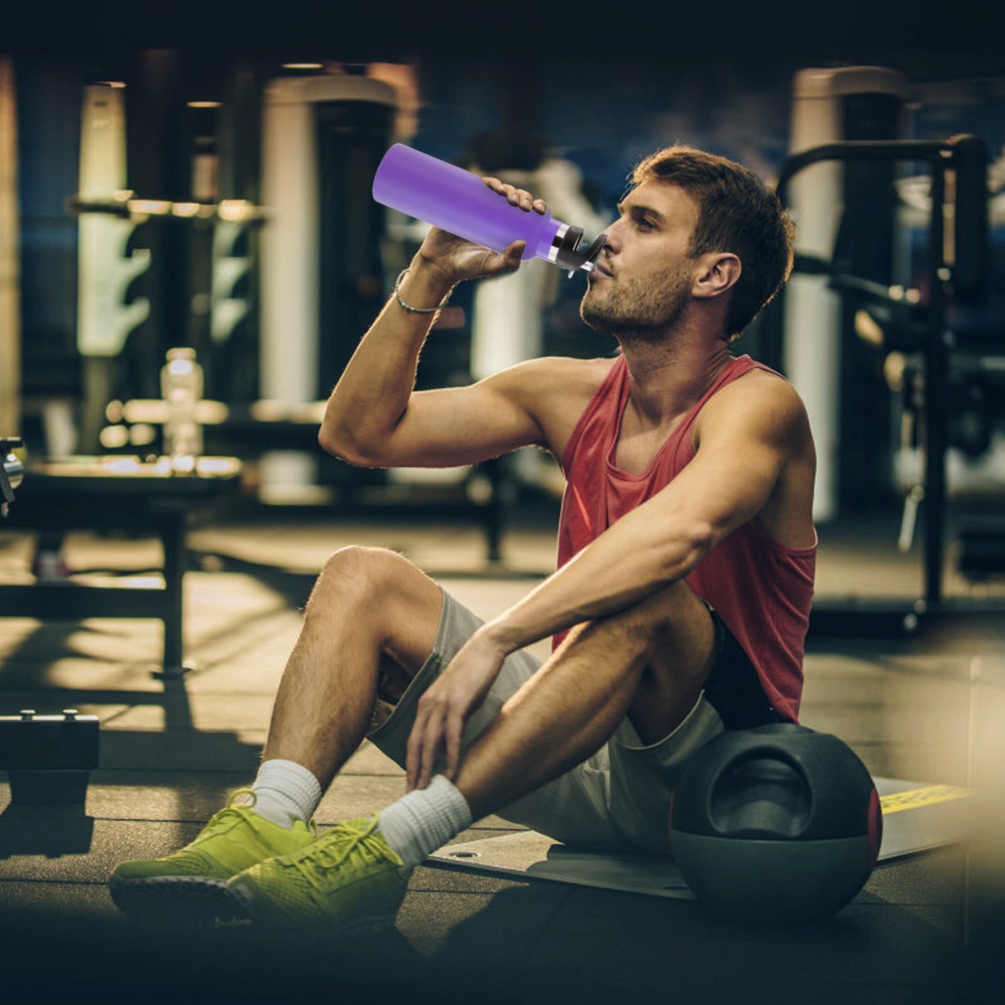 Man in a gym sitting on a weight bench, drinking from a purple water bottle.