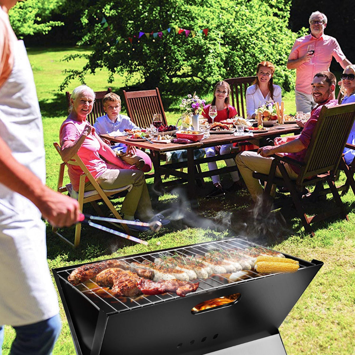 People enjoying a barbecue outdoors with food on a grill and a table in the background.