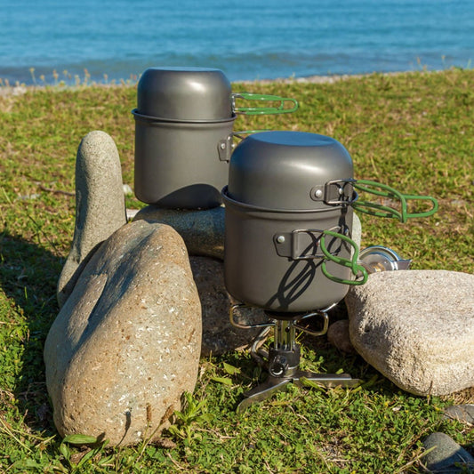 Two stacked aluminum camping pots on portable stove set among shoreline rocks