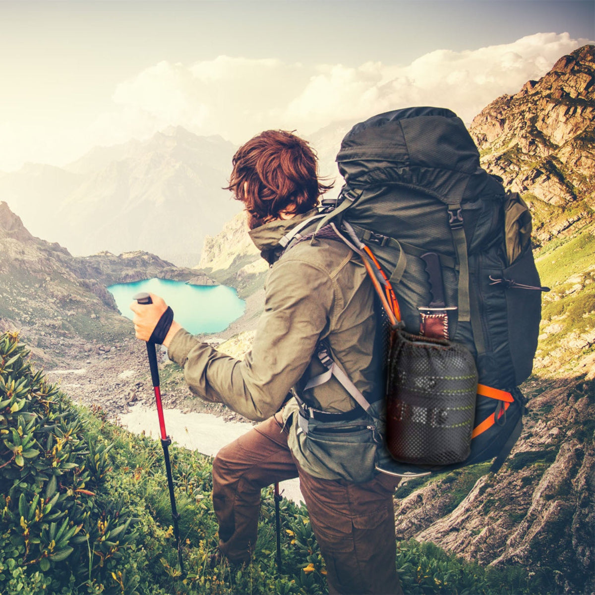 Person hiking with a large backpack and trekking poles, overlooking a scenic mountain landscape with a lake.