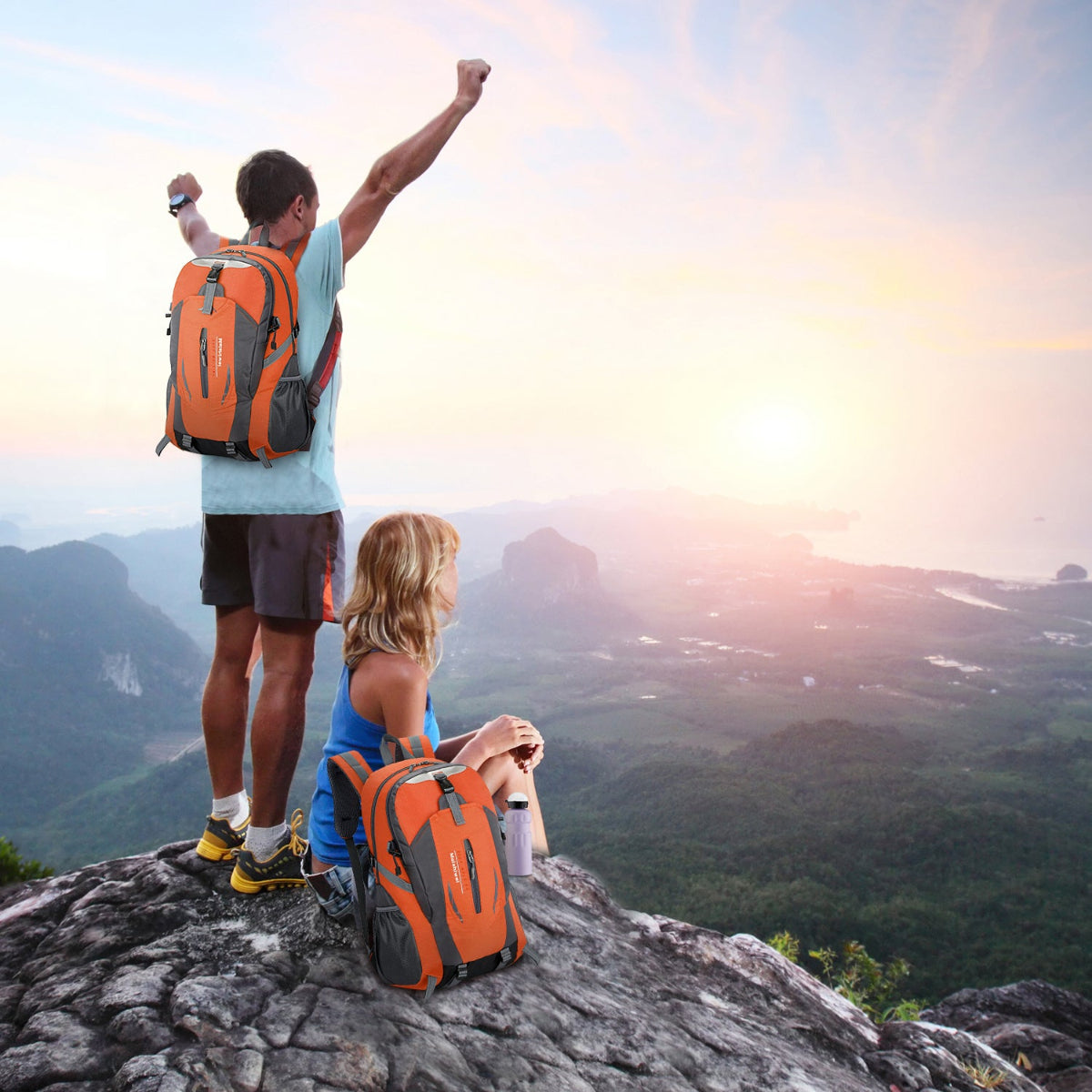 Two hikers with orange backpacks celebrating on a mountain top with a scenic view.