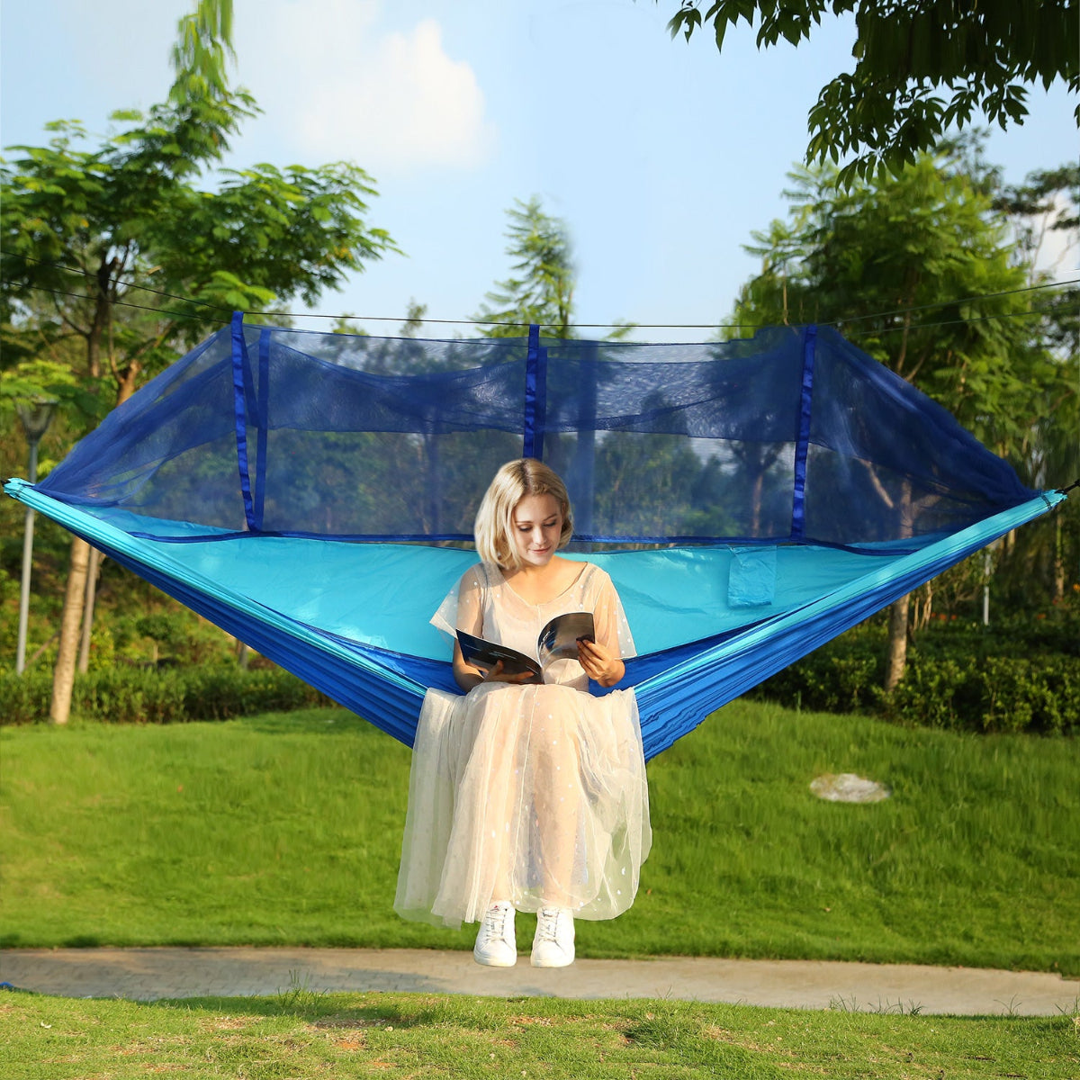 Woman sitting in a blue hammock with mosquito net in a park