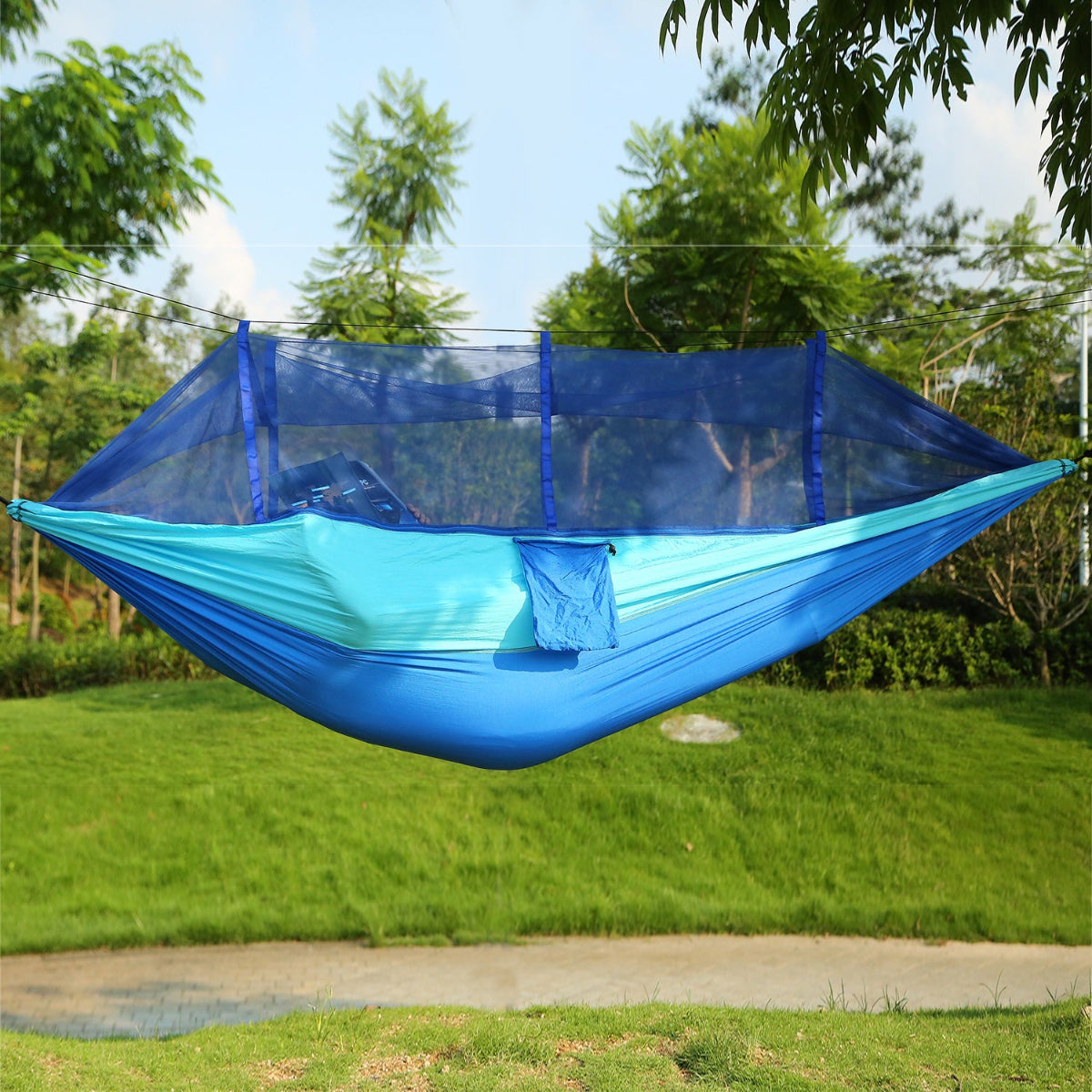 Blue hammock with mosquito net hanging outdoors on a sunny day.
