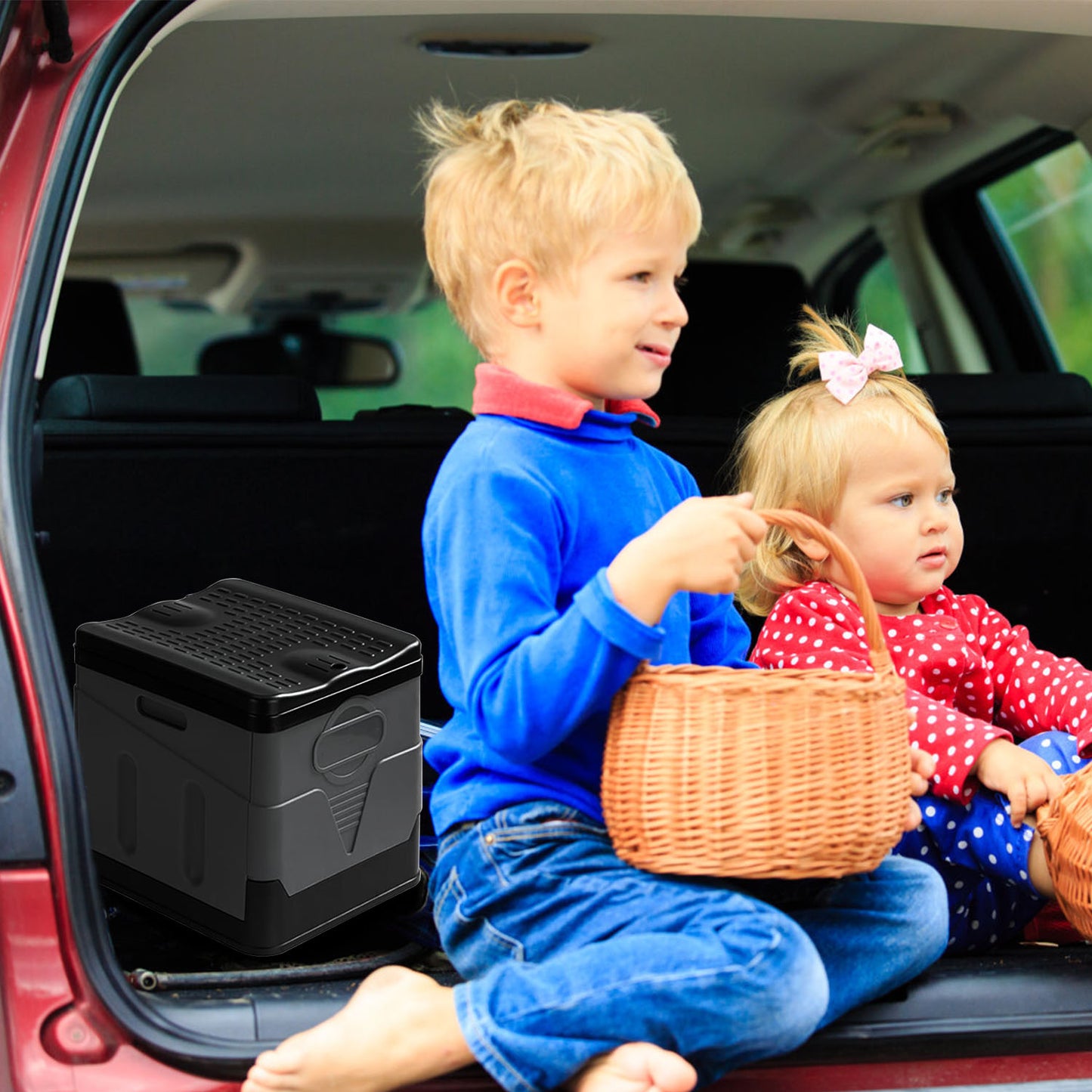Two children sitting in a car trunk with a cooler and a basket.