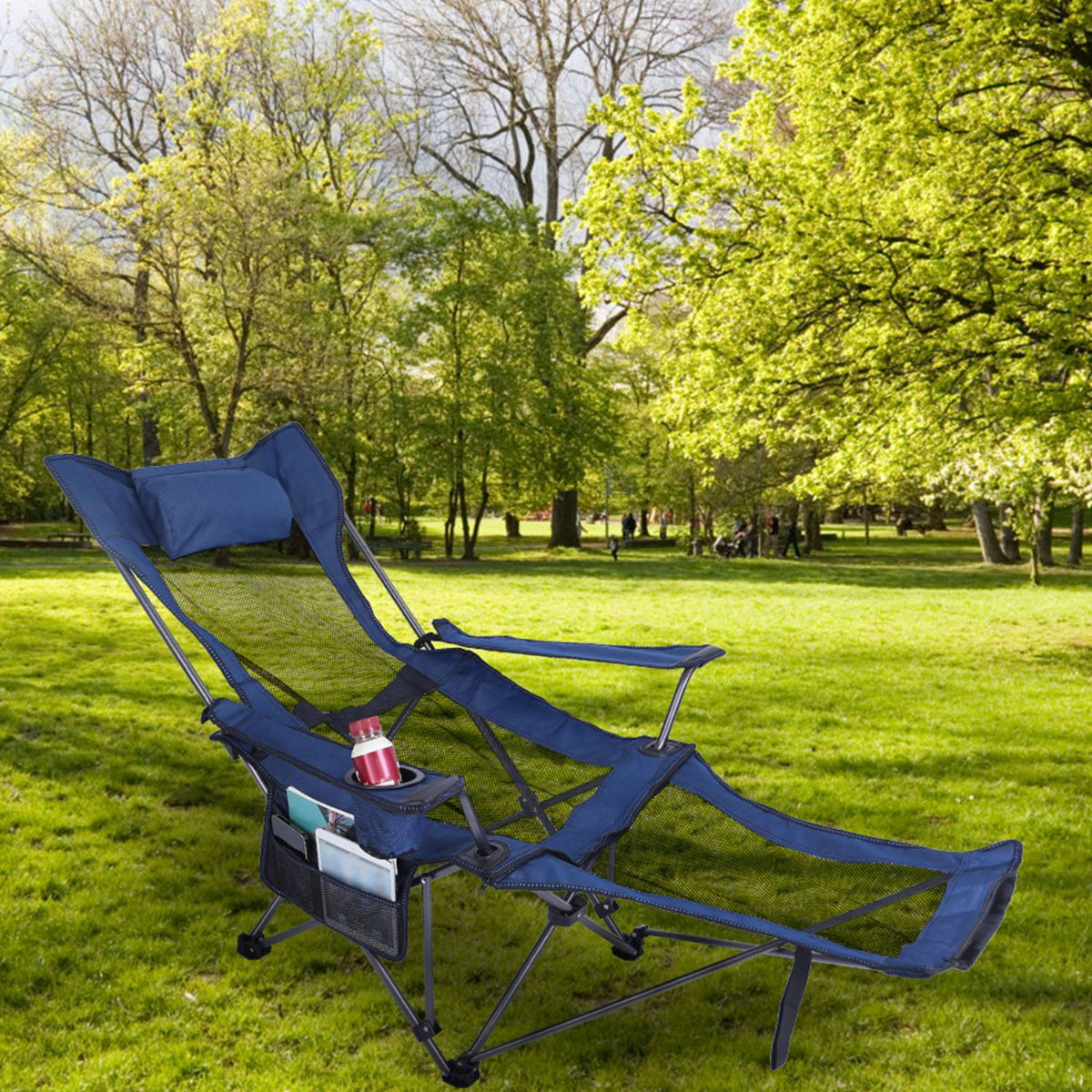Blue camping chair with cup holder and pillow on a grassy field with trees in the background