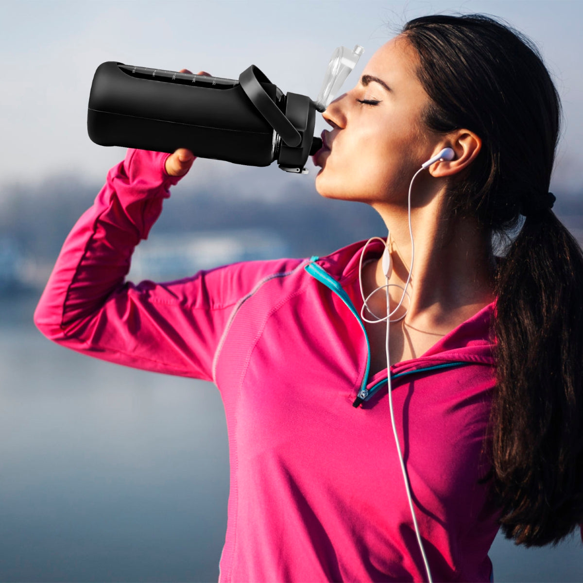 Woman drinking from black water bottle outdoors near water