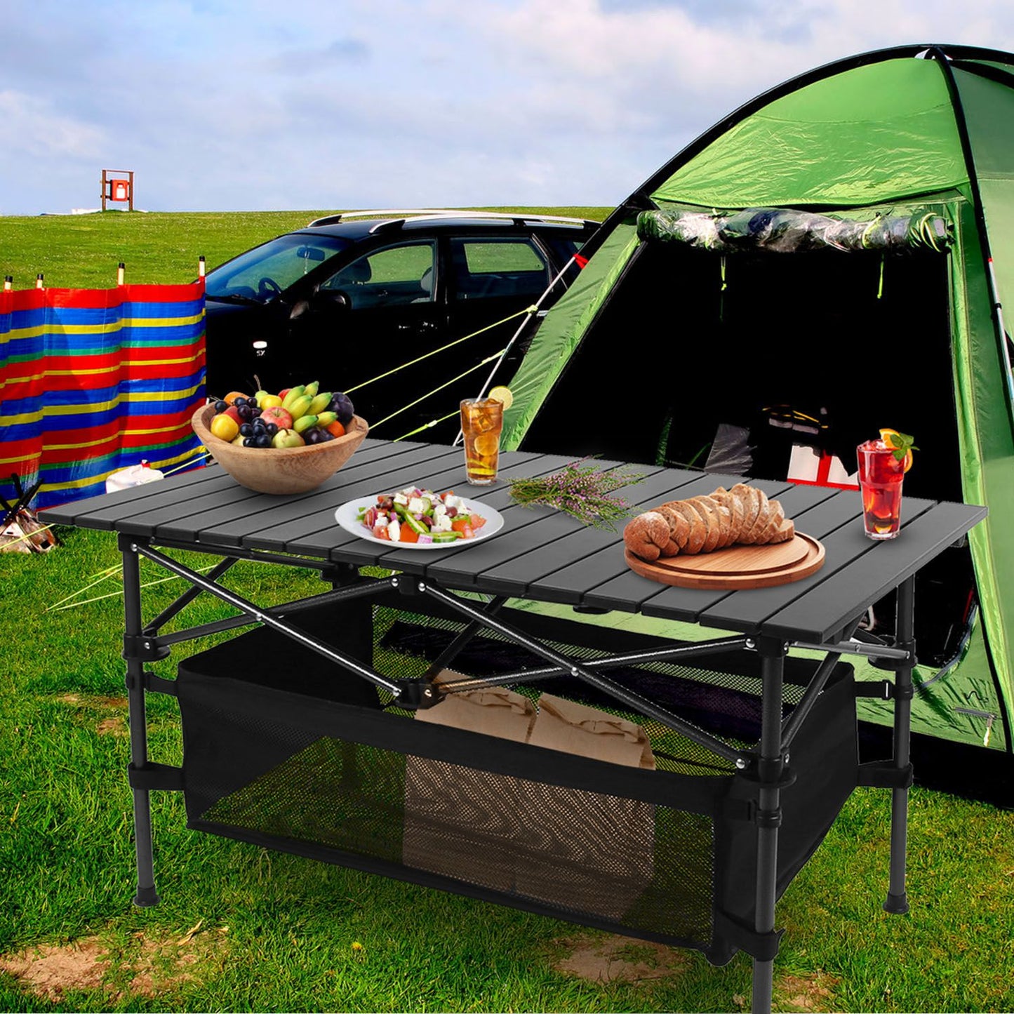 Camping scene with a table set for a picnic, tent, and car in the background.