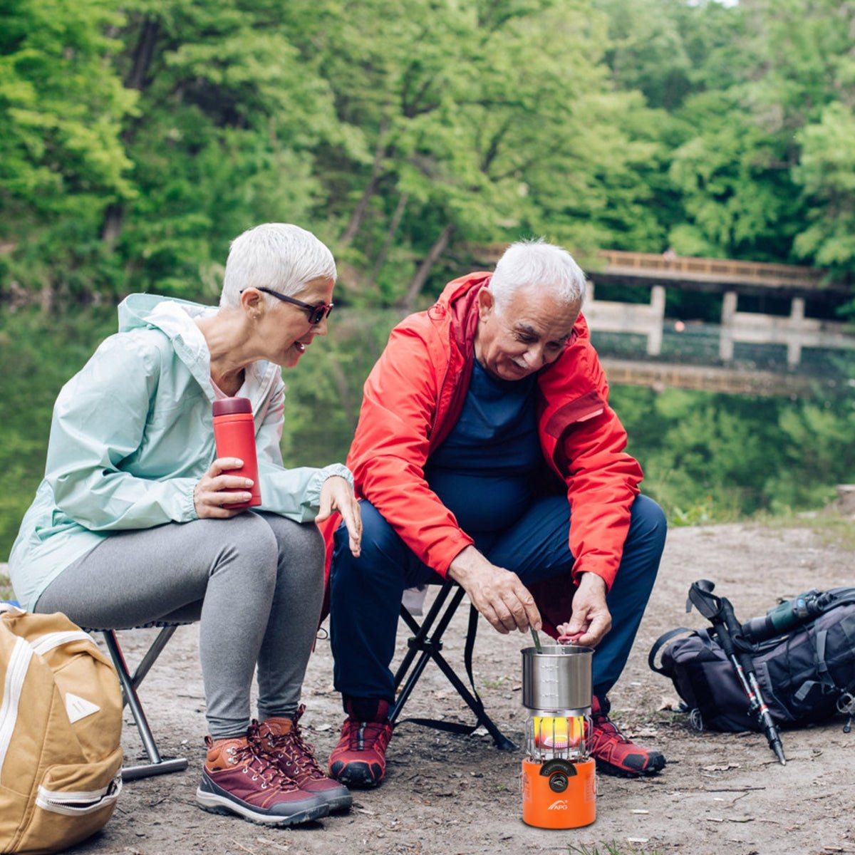 Camping stove heater operating beside seated adults near a lakeside campsite