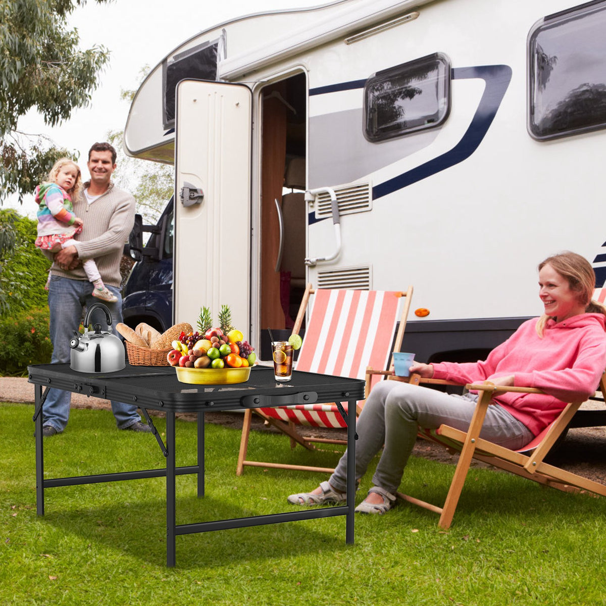 Family enjoying a picnic in front of an RV on a grassy area.
