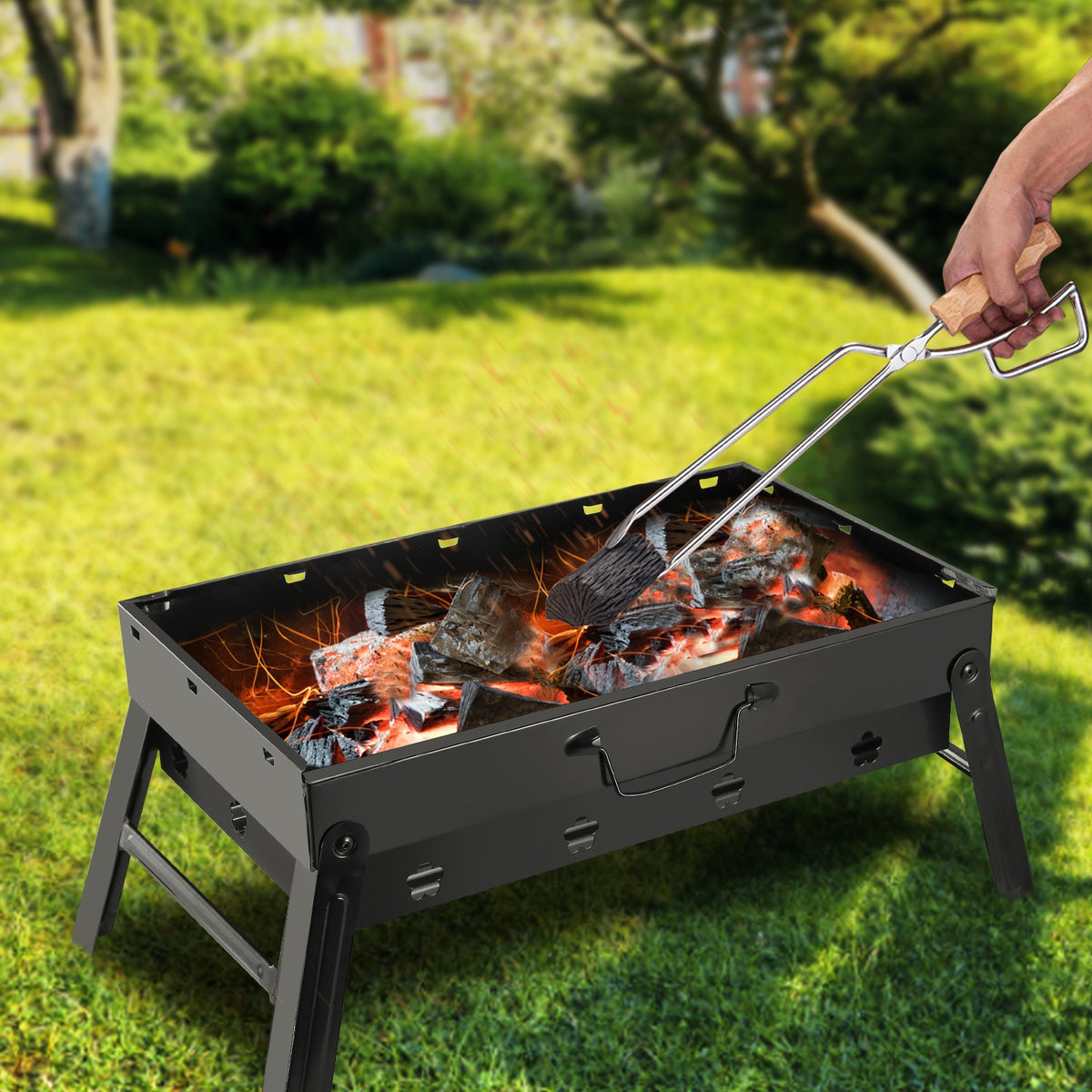Person using tongs to tend to a portable grill on grass