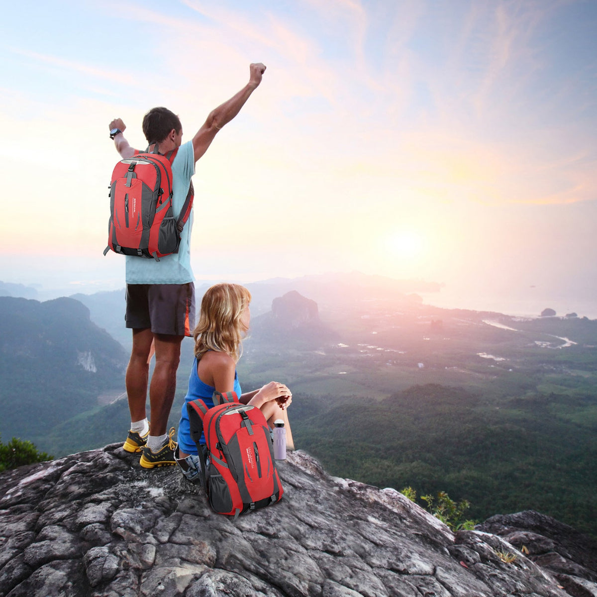Two hikers with backpacks standing on a mountain peak with a scenic view.