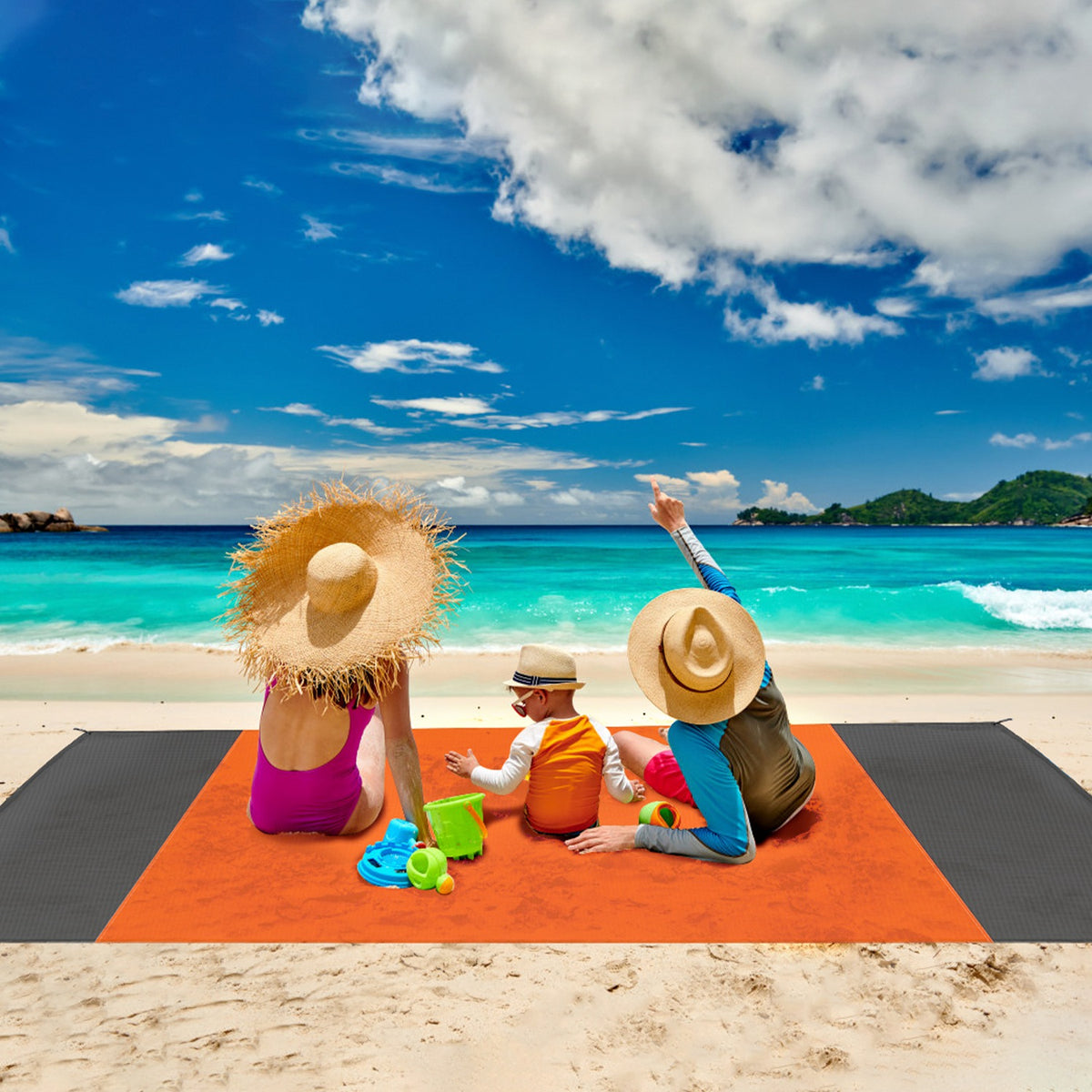 Family of three with sun hats sitting on an orange towel at the beach.