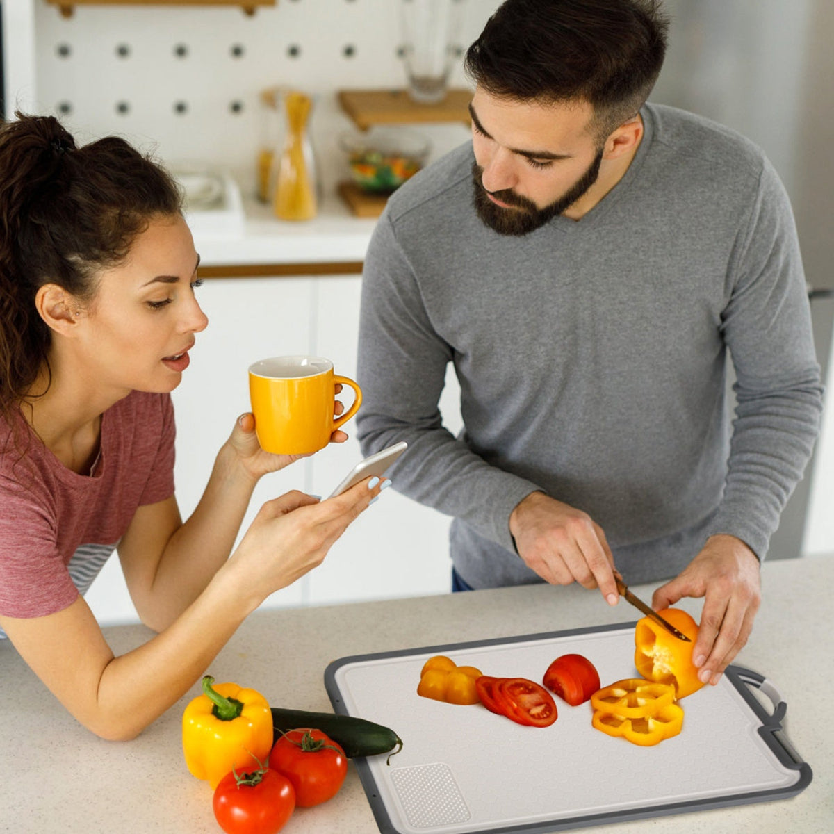 Man and woman in a kitchen with vegetables on a cutting board and a woman holding a yellow mug.