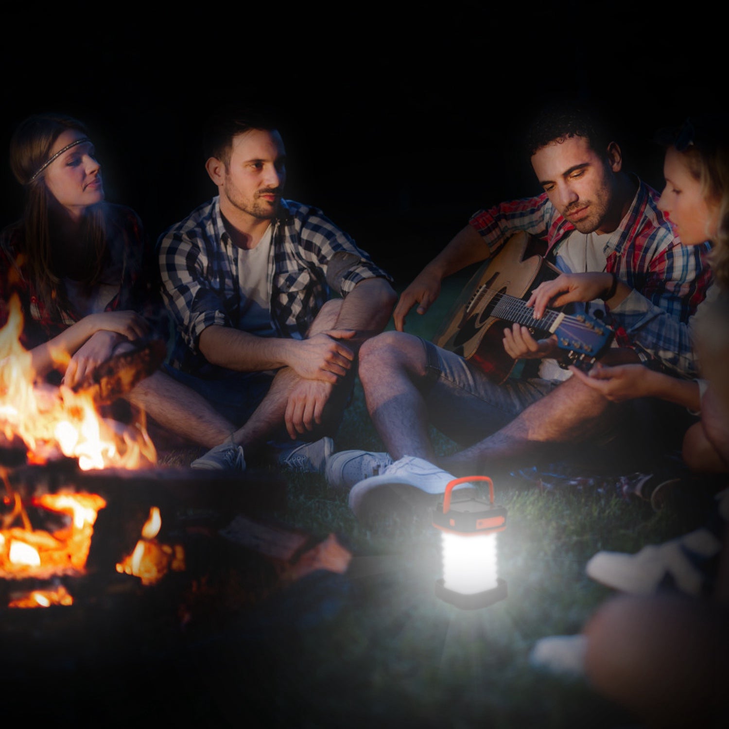 Group of people sitting around a campfire at night, with one person playing guitar.