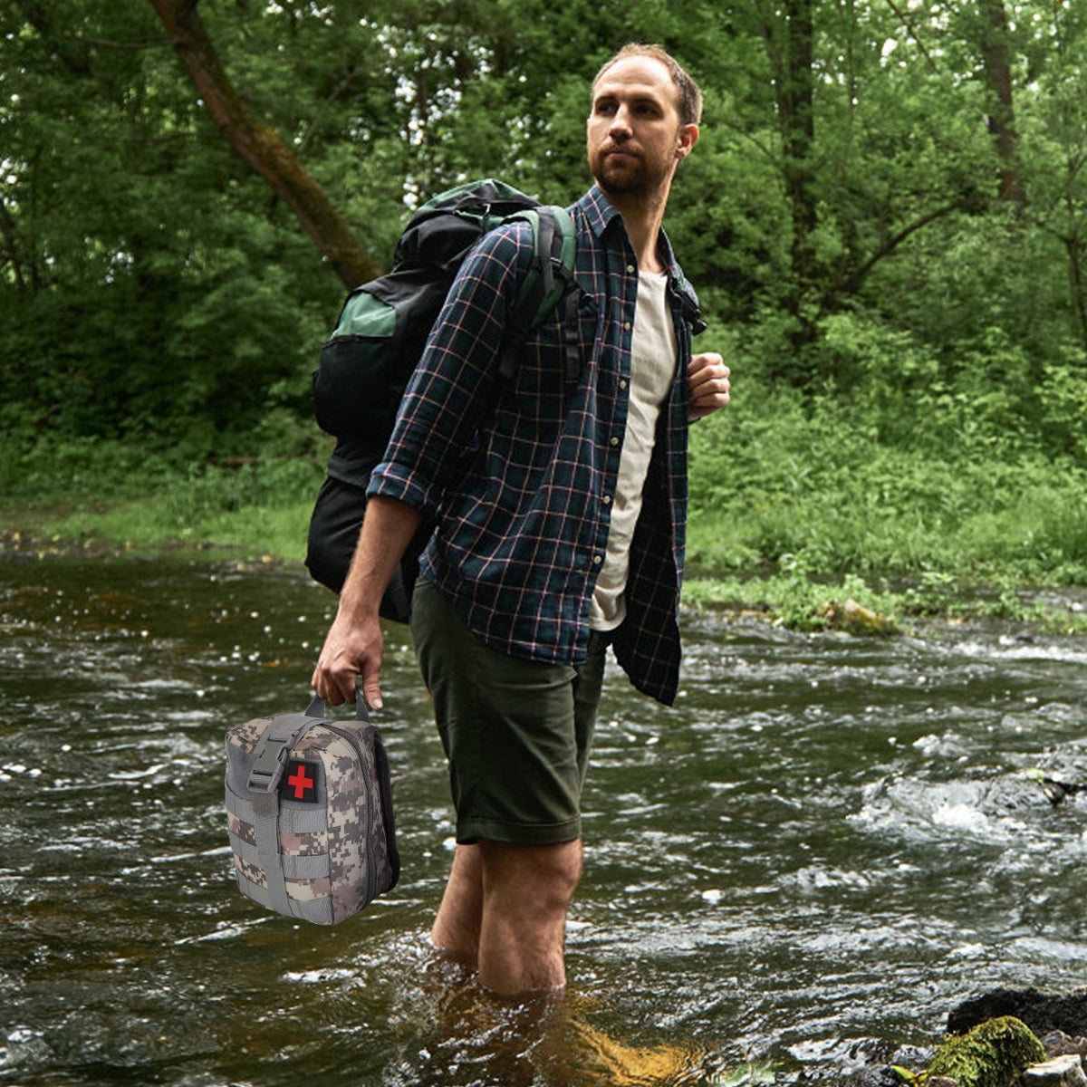 Man crossing a river with a backpack and a bag, surrounded by greenery.