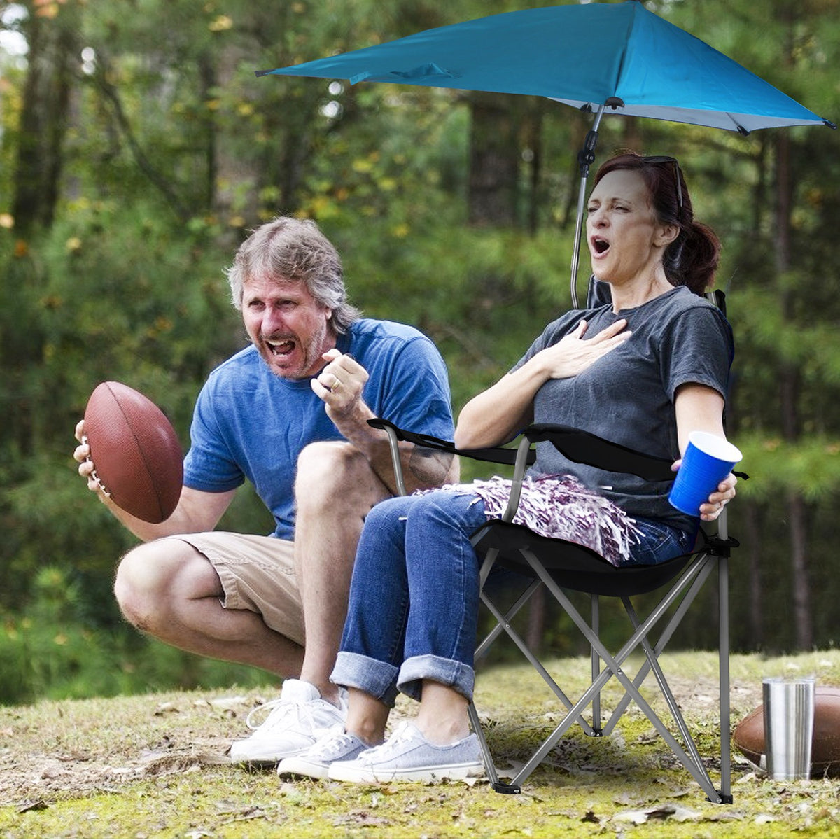 Two people sitting outdoors with a blue umbrella, one holding a football and the other a cup.