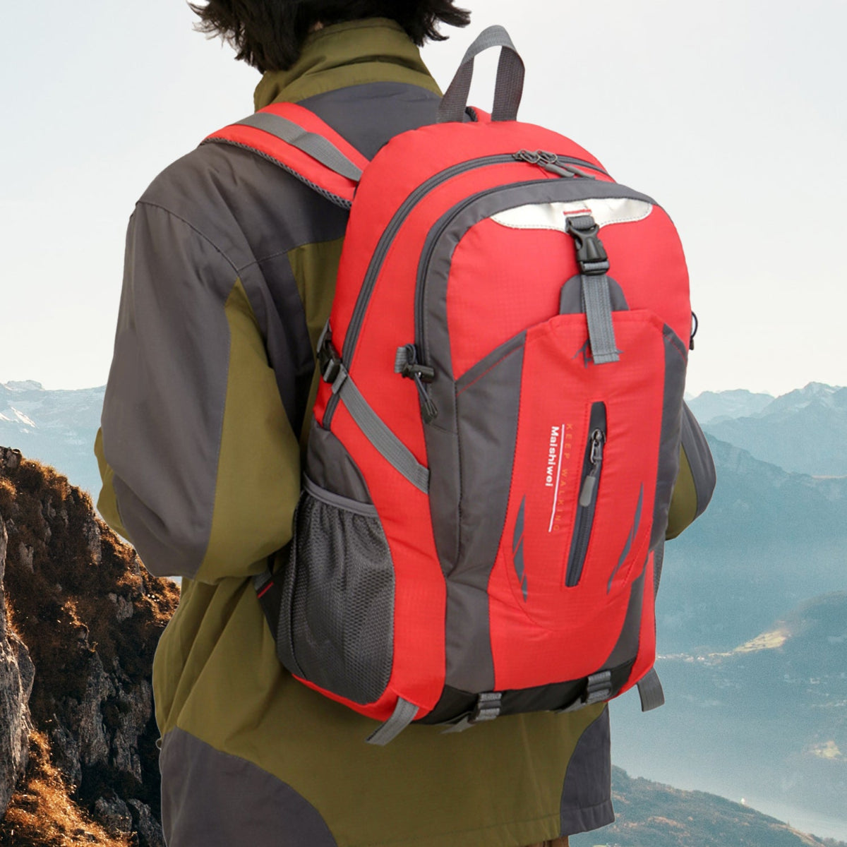 Person wearing a red and gray backpack with a mountainous landscape in the background