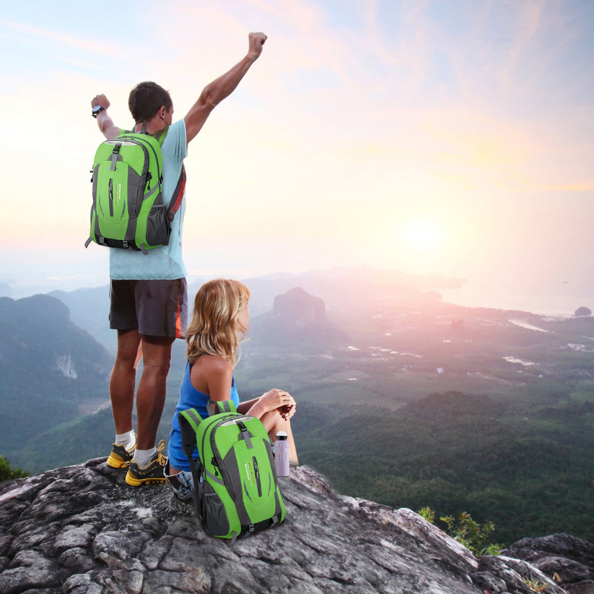 Two hikers with green backpacks enjoying a view of mountains at sunset.