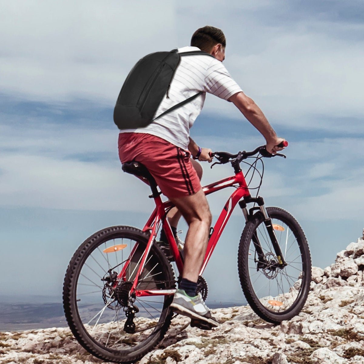 Person cycling uphill on rocky terrain wearing a slim black daypack