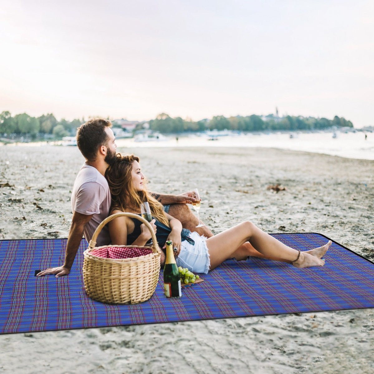 Picnic blanket on sandy beach with two people seated and basket nearby