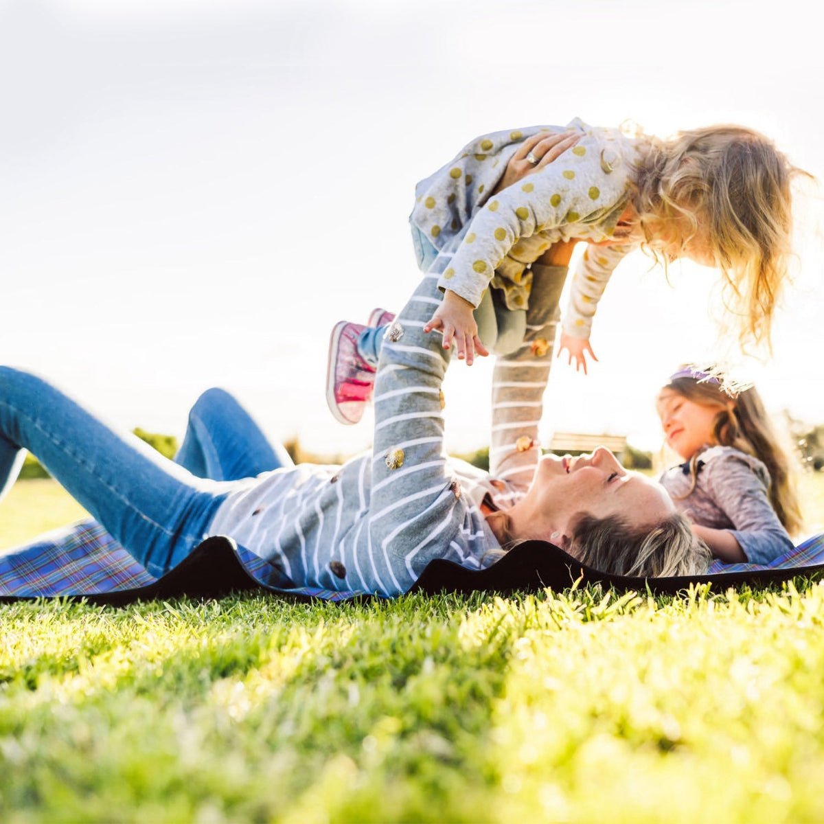 Adult lying on picnic blanket while lifting a child outdoors on grass