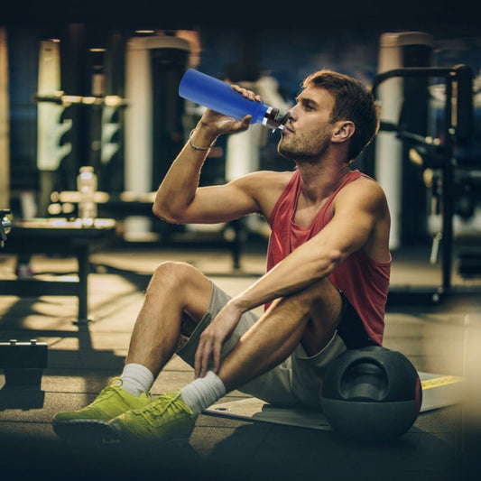 Person seated indoors drinking from blue stainless steel water bottle