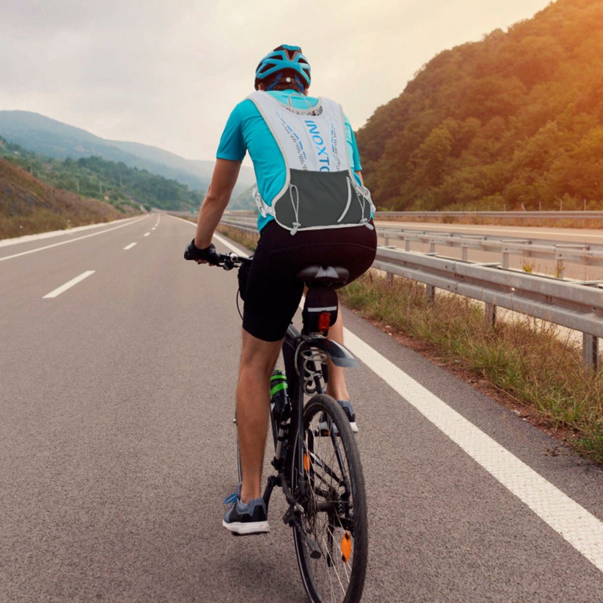 Person cycling outdoors wearing a light-colored hydration vest, viewed from behind