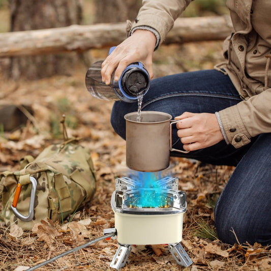 Backpacking stove heating a metal cup on forest ground beside camping gear
