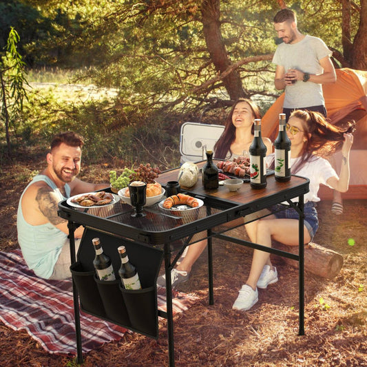 Camping table set outdoors with food and drinks beside tents and seated people